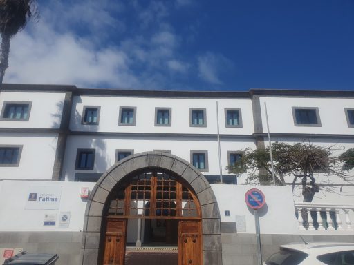 Edificio blanco con puertas de madera y ventanas, bajo un cielo azul.