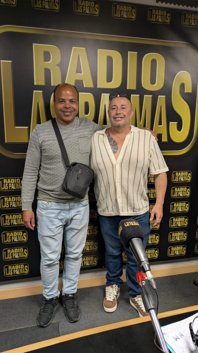 Dos hombres sonrientes posan juntos frente a un fondo de radio.
